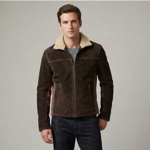 Può includere: Giacca in pelle scamosciata marrone con colletto in montone color crema. La giacca presenta una chiusura con zip, due tasche laterali e cuciture marroni. Le maniche e i lati hanno un pannello marrone a contrasto. Il modello indossa una maglietta grigia e jeans blu scuro.