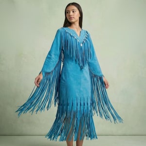 May include: A turquoise suede dress with long sleeves and a V-neck. The dress features long fringe detailing on the sleeves, neckline, and hem. The dress is knee-length and has a flowing silhouette.