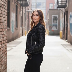 May include: A black motorcycle jacket featuring a textured, studded surface, a notched collar, and silver-toned metal zippers. The jacket is worn with plain black trousers, creating a monochromatic look with a focus on the detailed, raised embellishments.