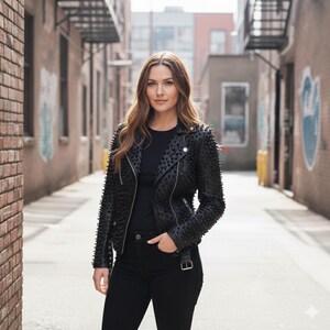May include: A black leather motorcycle jacket featuring an all-over studded design, silver-tone metal zippers, a notched lapel, and an adjustable waist belt with a buckle, worn over a plain black t-shirt and black denim jeans.