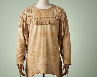 Könnte beinhalten: Ein beiges Langarm-Pulloverhemd aus wildlederartigem Material mit langen Fransen an Schultern, Ärmeln und Seiten. Der Brustbereich ist mit einem horizontalen Fransenpanel und zwei kreisförmigen, rot-weißen Perlenapplikationen versehen.
