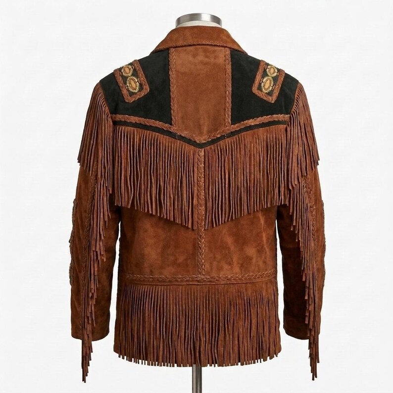 K&ouml;nnte beinhalten: Eine braune Wildlederjacke mit langen Fransen am R&uuml;cken und an den &Auml;rmeln. Das Kleidungsst&uuml;ck verf&uuml;gt &uuml;ber schwarze Wildledereins&auml;tze an den Schultern mit dekorativen kreisf&ouml;rmigen Stickereien, geflochtenen Lederverzierungen und einer R&uuml;ckenpasse.