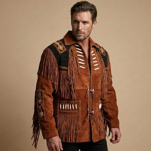 K&ouml;nnte beinhalten: Eine braune Wildlederjacke mit langen Fransen, schwarzen Schulterpartien und wei&szlig;en knochenartigen Verzierungen. Das Kleidungsst&uuml;ck verf&uuml;gt &uuml;ber geflochtene Lederbes&auml;tze, dekorative Stickereien an den &Auml;rmeln und vordere Schn&uuml;rverschl&uuml;sse.
