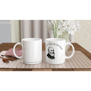 Könnte beinhalten: Zwei weiße Keramik-Kaffeetassen. Eine Tasse zeigt ein Schwarz-Weiß-Porträt eines Mannes mit dem Text "CAFFEINE RESPONSE". Die andere Tasse ist leer. Beide Tassen stehen auf einer karierten Oberfläche.