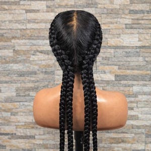 Könnte beinhalten: Ein Schaufensterpuppenkopf mit einer schwarzen geflochtenen Frisur. Die Zöpfe sind in einem französischen Zopfmuster geflochten, beginnend am Oberkopf und sich in vier lange, dicke Zöpfe erstreckend. Der Hintergrund ist eine strukturierte, hellbraune Backsteinmauer.