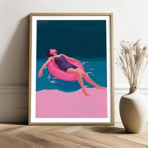 May include: A framed art print depicts a person relaxing in a pink inflatable ring in a pool. The person is wearing a dark blue swimsuit. The water is a teal color, and the background is a dark blue. The bottom of the image is a solid pink.