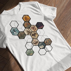 May include: White t-shirt featuring a geometric design of hexagonal patches with various illustrations. The patches depict cryptids and mythical creatures, including Bigfoot and Mothman. The shirt is made of a soft, comfortable material.