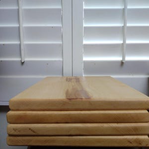 May include: A stack of four rectangular light-coloured wooden boards with smooth surfaces and visible natural wood grain patterns. The boards are stacked neatly on top of each other, showcasing the light tan colour and the texture of the wood.