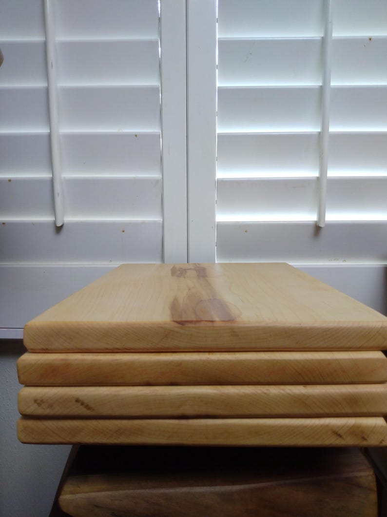 May include: A stack of four rectangular light-coloured wooden boards with smooth surfaces and visible natural wood grain patterns. The boards are stacked neatly on top of each other, showcasing the light tan colour and the texture of the wood.