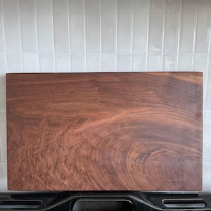 Op de afbeelding: Een rechthoekige houten snijplank met een rijke, donkerbruine kleur en zichtbare natuurlijke houtnerfpatronen. Het oppervlak is glad en vlak, wat de organische textuur en de diepe tinten van het hout over het hele stuk laat zien.