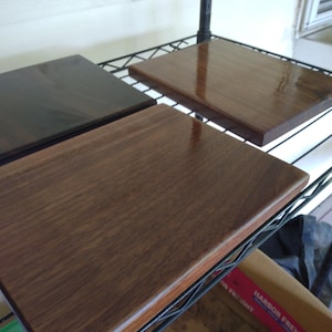 Op de afbeelding: Drie rechthoekige houten planken met een gladde, gepolijste afwerking. De planken vertonen zichtbare houtnerfpatronen in verschillende tinten donkerbruin en walnoot, met afgeronde randen en een glanzend, reflecterend oppervlak.