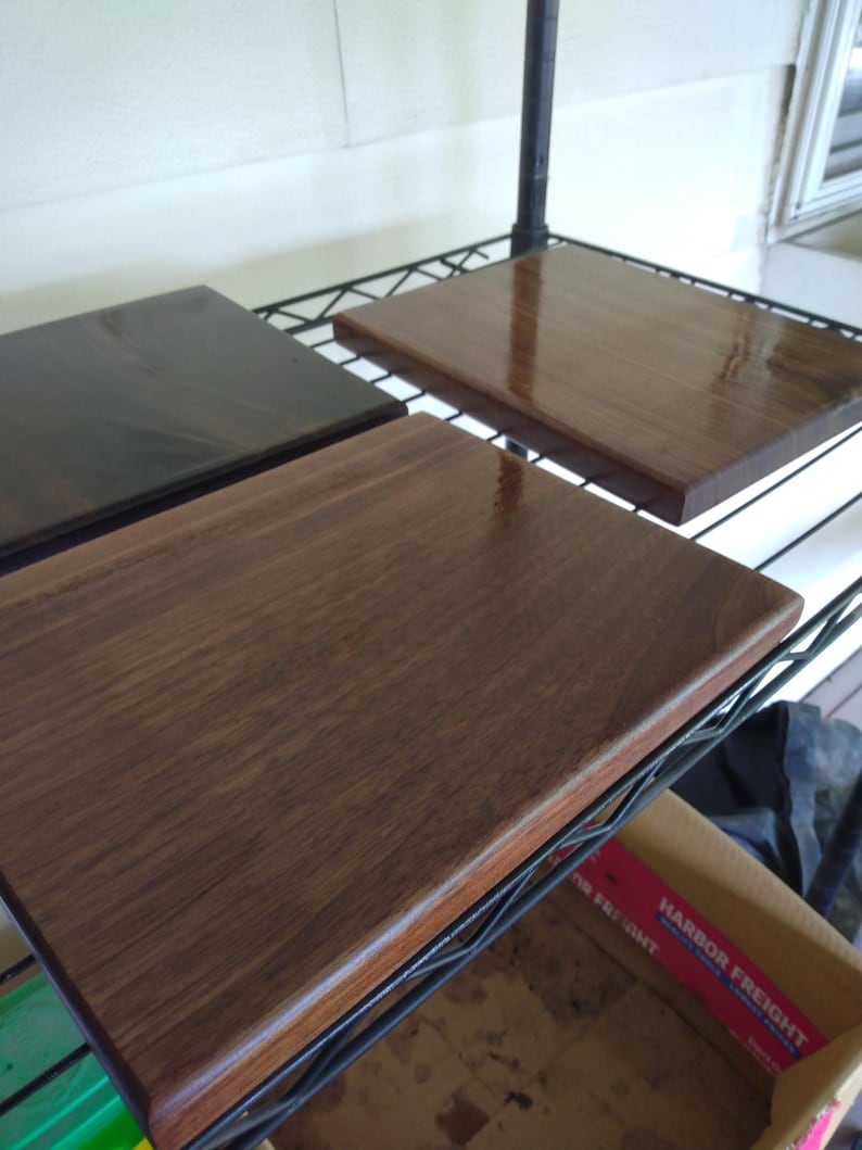 Op de afbeelding: Drie rechthoekige houten planken met een gladde, gepolijste afwerking. De planken vertonen zichtbare houtnerfpatronen in verschillende tinten donkerbruin en walnoot, met afgeronde randen en een glanzend, reflecterend oppervlak.