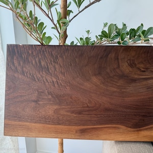 Op de afbeelding: Een rechthoekige houten snijplank met een rijke, donkerbruine nerf, wervelende natuurlijke houtstructuren en een glad, gepolijst oppervlak. De plank heeft een diepe walnootkleur met lichtere bruintinten langs de onderste rand.