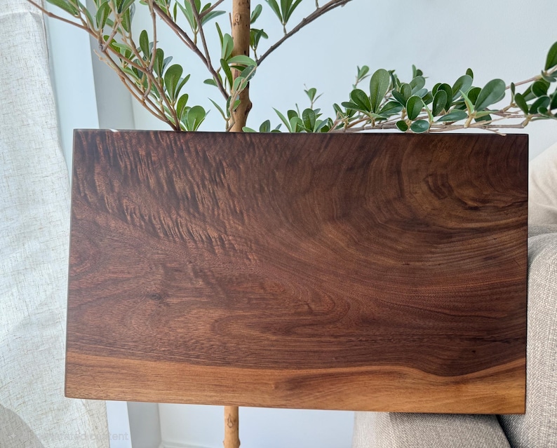 Op de afbeelding: Een rechthoekige houten snijplank met een rijke, donkerbruine nerf, wervelende natuurlijke houtstructuren en een glad, gepolijst oppervlak. De plank heeft een diepe walnootkleur met lichtere bruintinten langs de onderste rand.