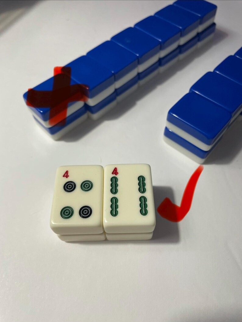 May include: A set of rectangular mahjong tiles with blue and white backs, arranged in rows. Two cream-colored tiles are placed in the foreground, one showing four black and green circular symbols with a red number four, and one showing two green bamboo-like symbols with a red number four.