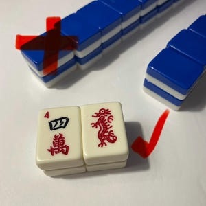 May include: A set of rectangular mahjong tiles with blue backs and white fronts. Two tiles are placed in the foreground: one features the number 4 and Chinese characters in red and black, and the other displays a red dragon illustration.