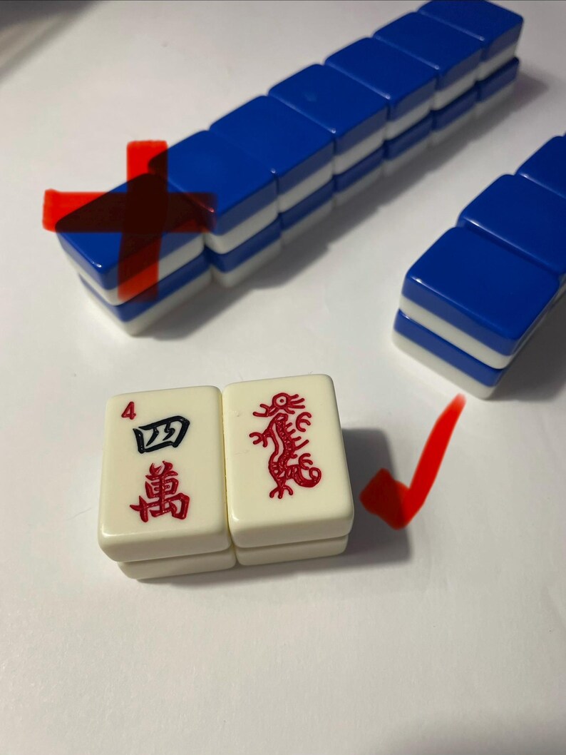 May include: A set of rectangular mahjong tiles with blue backs and white fronts. Two tiles are placed in the foreground: one features the number 4 and Chinese characters in red and black, and the other displays a red dragon illustration.