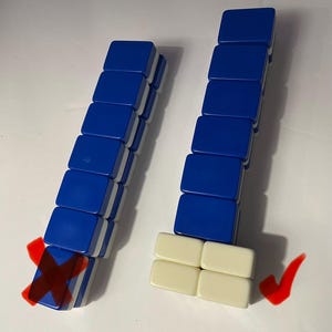 May include: Two vertical stacks of rectangular mahjong tiles. The left stack consists of six blue tiles with white backs, marked with a red X. The right stack features six blue tiles atop four cream-colored tiles, marked with a red checkmark.