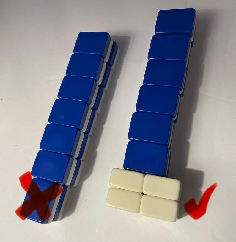 May include: Two vertical stacks of rectangular mahjong tiles. The left stack consists of six blue tiles with white backs, marked with a red X. The right stack features six blue tiles atop four cream-colored tiles, marked with a red checkmark.