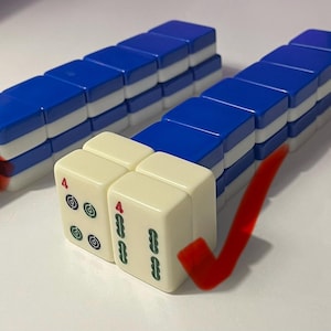 May include: Two rows of blue and white Mahjong tiles arranged in stacks. One row is marked with a red X, and the other row features two cream-colored tiles at the front, each displaying a red number 4 and green symbols, marked with a red checkmark.