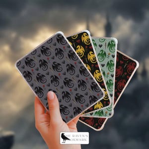 May include: Four phone cases with dragon patterns in various colors: gray, gold, green, and red. Each case features a repeating design of dragons, daggers, hearts, and roses. The cases are held in a hand against a blurred background.