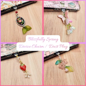 May include: Four device charms/dust plugs with floral and nature-inspired designs. One features a red strawberry, another a butterfly, and two with flowers. The text "Blissfully Spring Device Charm / Dust Plug" is displayed in the center.