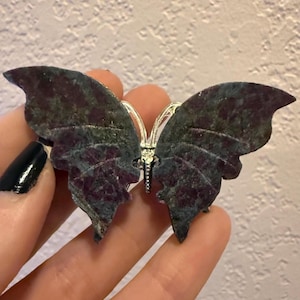 May include: A butterfly-shaped ornament crafted from dark green and deep red mottled stone, featuring a central silver-toned metal body with delicate antennae. The wings display a natural, textured surface with irregular color patterns throughout.