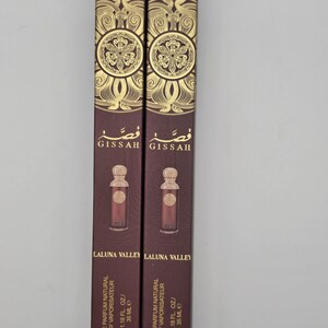 May include: Two rectangular perfume boxes in a vertical arrangement. The boxes are a deep burgundy color with gold decorative patterns and text. The boxes contain a perfume bottle with a matching burgundy color. The text on the box reads "GISSAH" and "LALUNA VALLEY".