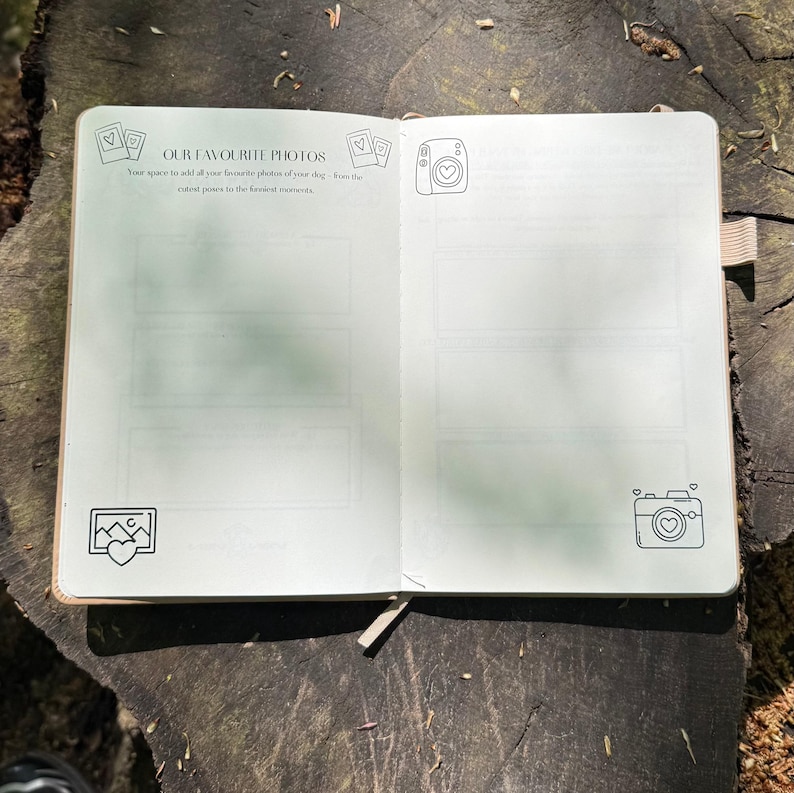 Op de afbeelding: Open notitieboek met de tekst "OUR FAVOURITE PHOTOS" en ruimte voor foto's. Het notitieboek heeft lijntekeningen van camera's en harten. Het notitieboek ligt open op een houten oppervlak.