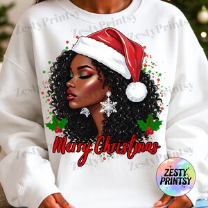 May include: White sweatshirt featuring a graphic of a Black woman wearing a Santa hat and snowflake earrings. The design includes the text "Merry Christmas" in red script, with green and red accents. The Zesty Prints logo is in the lower right corner.
