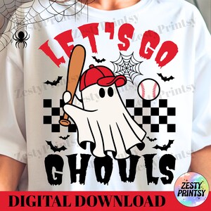 May include: White t-shirt with a Halloween-themed graphic. The design features a ghost wearing a red baseball cap and holding a bat, with the words "LET'S GO GHOULS" in red and black. A baseball and bats are also included.