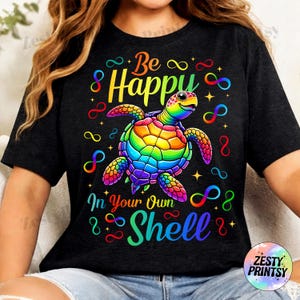 May include: Black t-shirt with a colorful turtle graphic. The turtle has a rainbow shell and is surrounded by infinity symbols and stars. Text on the shirt reads "Be Happy In Your Own Shell."