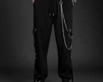 May include: Black cargo pants with a drawstring waist, side pockets, and silver chain detail. The pants have straps and metal accents. The person is wearing black and white sneakers.