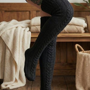 May include: Dark gray, cable-knit over-the-knee socks. The socks have a ribbed texture on the leg and a cable-knit design on the upper thigh. The socks are made of a thick, warm material, perfect for cold weather.
