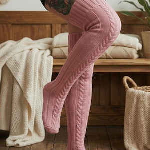 May include: Pink cable knit over-the-knee socks. The socks have a ribbed texture on the foot and a cable knit design up the leg. The socks are made of a soft, warm material.