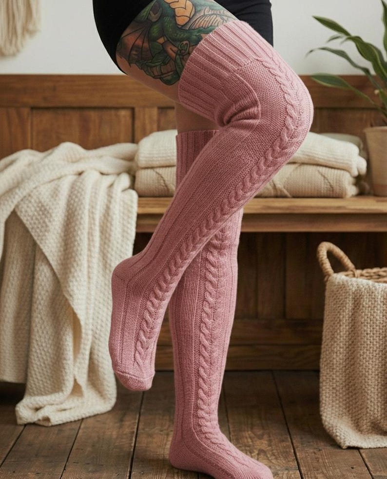 May include: Pink cable knit over-the-knee socks. The socks have a ribbed texture on the foot and a cable knit design up the leg. The socks are made of a soft, warm material.