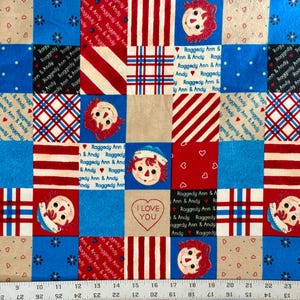 May include: A patchwork fabric featuring squares with Raggedy Ann and Andy faces, hearts, stripes, and the text "I Love You." The color scheme includes red, blue, and cream, creating a nostalgic, vintage feel. The fabric is suitable for quilting and crafting.