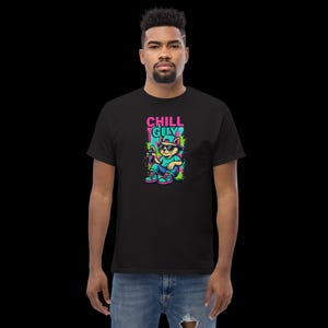 Könnte beinhalten: Schwarzes T-Shirt mit einem Cartoon-Katzen-Design. Die Katze trägt eine Sonnenbrille und hält ein Getränk. Der Text "CHILL GUY" ist in Pink und Türkis. Die Katze ist in einer entspannten Pose.