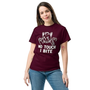 Könnte beinhalten: Ein weinrotes T-Shirt mit einer weißen Katzenzeichnung und dem Text "NO TOUCH I BITE". Die Katze hat einen wütenden Gesichtsausdruck und einen Stachelhalsband. Das T-Shirt ist aus weichem Material.
