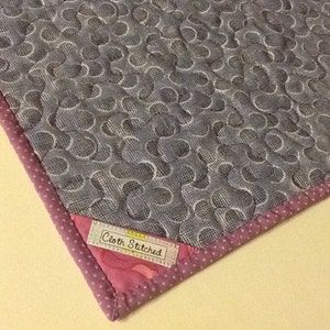 Puede incluir: Textil acolchado con un patr&oacute;n gris y blanco de c&iacute;rculos entrelazados. El borde est&aacute; adornado con una tela rosa de lunares y un borde rosa. La etiqueta dice "Cloth Stitched".