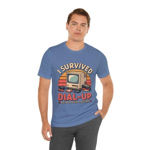 Puede incluir: Camiseta azul con un diseño gráfico de ordenador retro y el texto "I SURVIVED DIAL-UP RETRO TECH LEGEND". El diseño incluye un atardecer y antiguos periféricos de ordenador, en un estilo vintage.