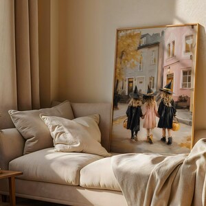 May include: A framed painting depicts three children in witch costumes walking down a street. The children wear black cloaks and hats, holding hands and carrying pumpkin-shaped baskets. The background shows buildings and autumn foliage.