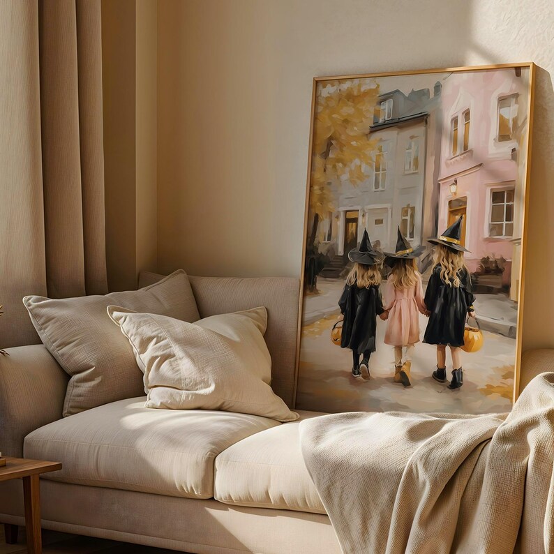 May include: A framed painting depicts three children in witch costumes walking down a street. The children wear black cloaks and hats, holding hands and carrying pumpkin-shaped baskets. The background shows buildings and autumn foliage.