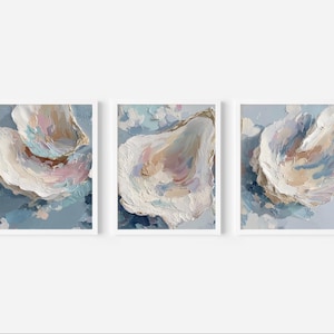 May include: Three framed abstract art prints. Each print features a close-up of an oyster shell in shades of white, beige, pink, and gold, set against a blue background. The artwork has a textured, painted appearance.