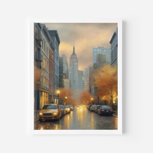May include: A framed watercolor painting of a New York City street scene. Yellow taxis line the wet street, with the Empire State Building visible in the distance. The artwork features muted colors, with autumn foliage and streetlights adding warmth.