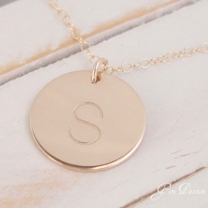 May include: Gold necklace with a round pendant featuring the letter "S" engraved on it.