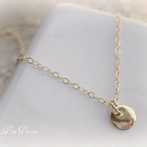 May include: A delicate gold chain necklace with a small, round pendant. The pendant is smooth and has a slightly hammered texture.