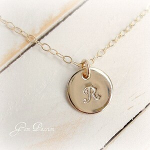 May include: A gold chain necklace with a round pendant featuring the letter "R" engraved on it.