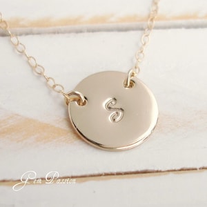 May include: Gold necklace with a round pendant featuring the letter "S" engraved on it.