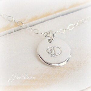 May include: A silver necklace with a round pendant featuring the letter "D" engraved on it.